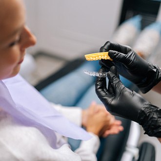 Orthodontist with black gloves removing clear aligner from model of teeth